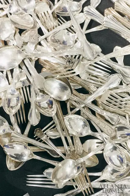 Close-up of a pile of antique silver spoons and forks with ornate handles.