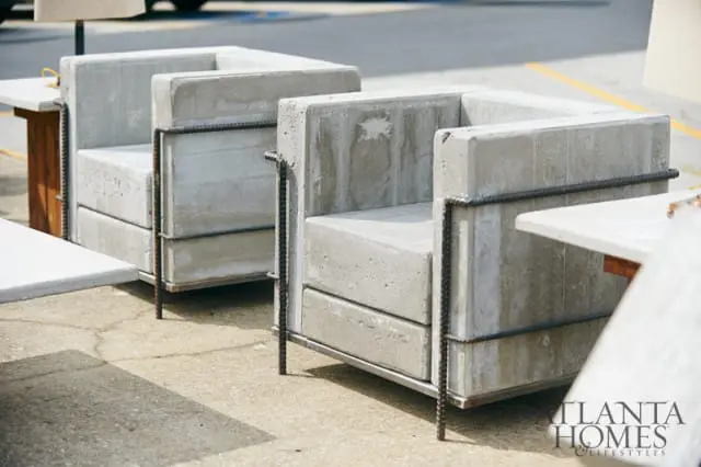 Two concrete armchairs with exposed rebar accents sit on a paved surface next to a table. The Atlanta Homes & Lifestyles logo is in the lower right corner.