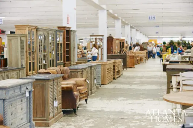 Wide shot of an indoor market with rows of antique furniture including cabinets, dressers, and chairs. People browse the merchandise in the background.