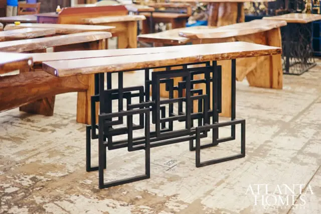 Live-edge wood console table with a geometric black metal base, displayed in a showroom with other wooden furniture.