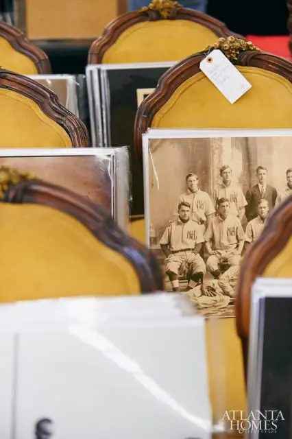 Antique chairs with yellow upholstery and ornate wood trim surround framed vintage photographs of a baseball team and other items.
