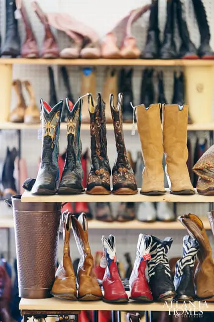 Shelves filled with various cowboy boots, including embroidered black and brown leather boots, tan suede boots, and red, white, and blue boots with zebra print accents.