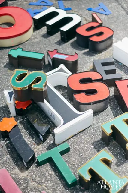 Assortment of vintage channel letters in various colors and sizes, including red O, white M, green S, and red S, scattered on asphalt.