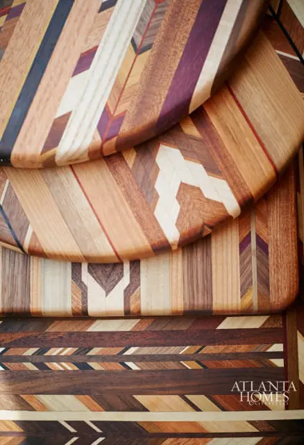 Stack of wooden cutting boards with geometric patterns made from various wood grains and colors, including light maple, dark walnut, and purple heart wood.