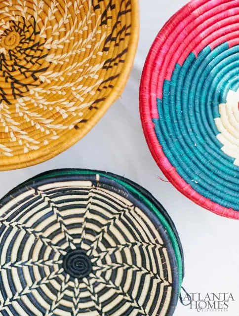 Three woven baskets with intricate patterns: one yellow with black and white, one pink and teal, and one black and white with a starburst design.