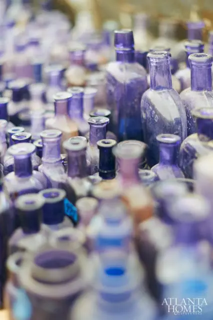 Close-up of a collection of antique purple glass bottles, many with dusty surfaces and varied neck shapes.
