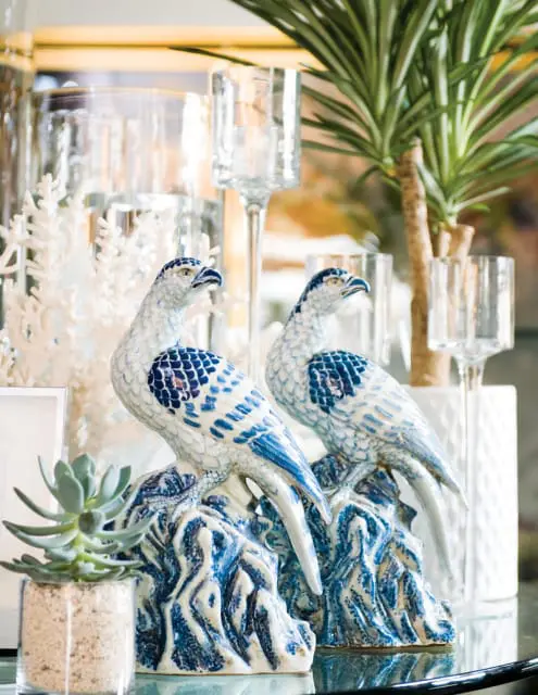 Two blue and white ceramic bird figurines perched on rocky bases, with a succulent plant and glass candle holders in the background.