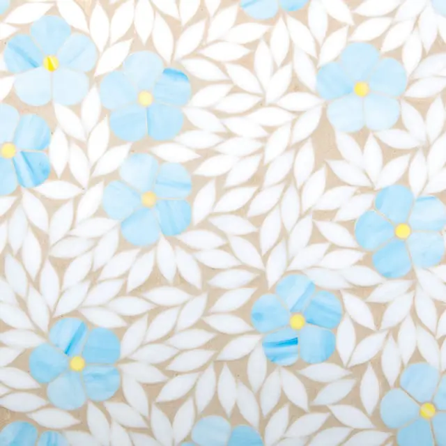 Mosaic tile with a pattern of light blue flowers with yellow centers and white leaves on a beige background.