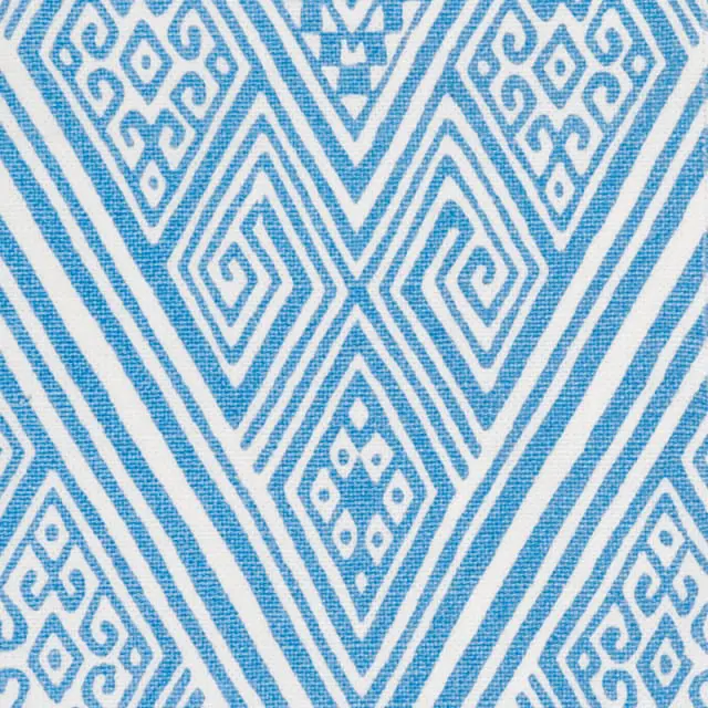 Close-up of a white fabric with a repeating geometric pattern in bright blue. The pattern features diamonds, zigzags, and spiral motifs.
