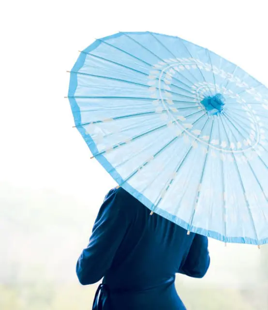 Close-up of a light blue paper parasol with white floral detailing, held by a person in a dark blue dress.