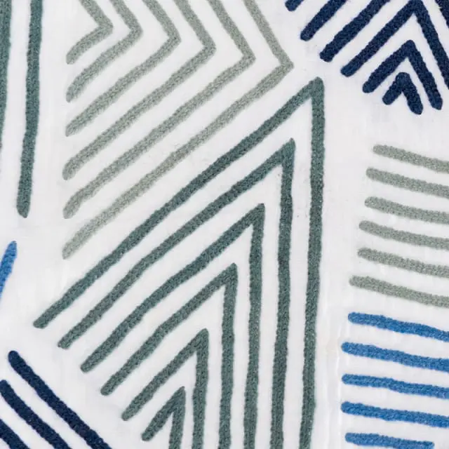 Close-up of white fabric with embroidered geometric patterns in shades of blue and green.