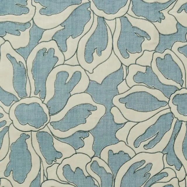 Close-up of light blue fabric with an embroidered floral pattern in cream and gray stitching.