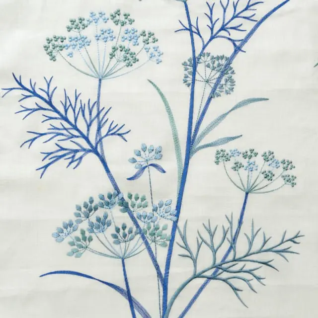 Close-up embroidery of blue and green dill flowers and stems on a cream linen background.