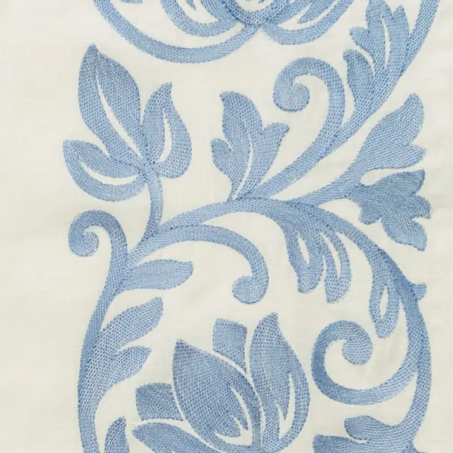 Close-up of light cream fabric with blue embroidered floral and scroll pattern.