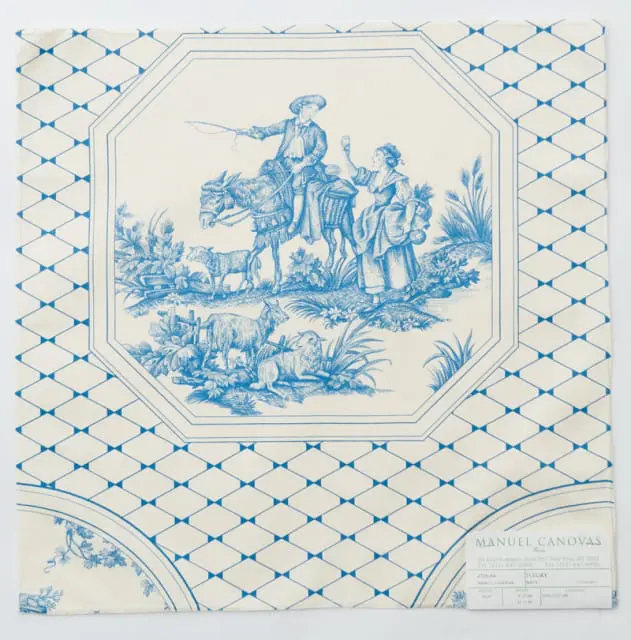 Blue and white toile fabric featuring a pastoral scene with a man on a donkey, a woman, sheep, and goats, bordered by a geometric pattern.