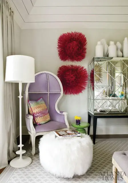 Purple velvet armchair with nailhead trim, chevron pillow, white floor lamp, and fluffy white ottoman topped with books.