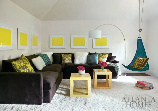Living room with a dark brown sectional sofa, white shag rug, yellow framed art, and a teal hanging chair.