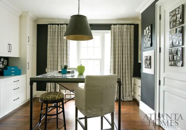 Craft room with dark gray walls, white custom cabinetry, a metal-top table with chairs, and patterned curtains.