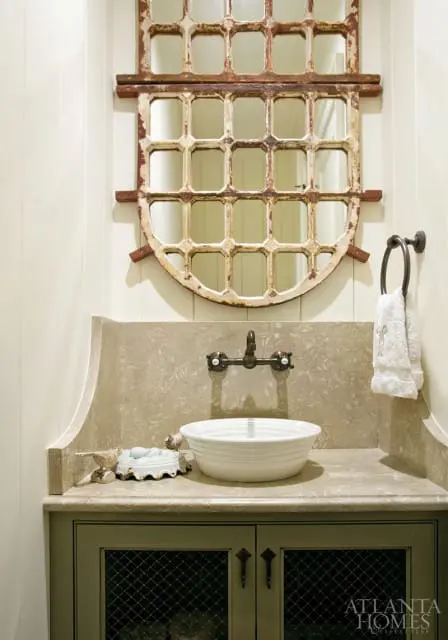 Powder room with a white vessel sink, stone countertop, antique window pane mirror, and green vanity with wire mesh doors.