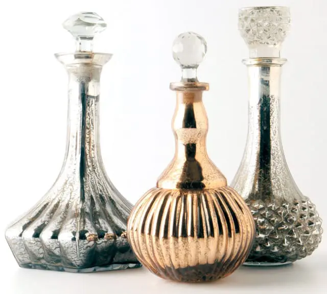 Three decorative glass decanters with stoppers: one copper-toned with vertical ribs, one silver with a faceted pattern, and one silver with a fluted base.