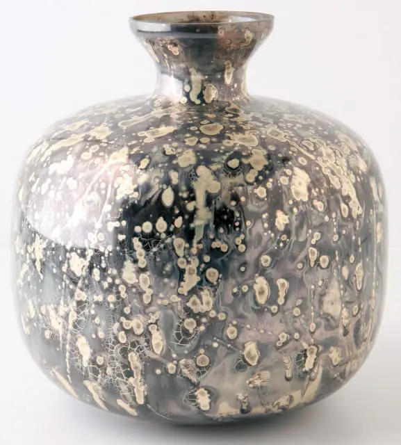 Round ceramic vase with a speckled, iridescent glaze in shades of black, grey, and cream, featuring a narrow neck and opening.