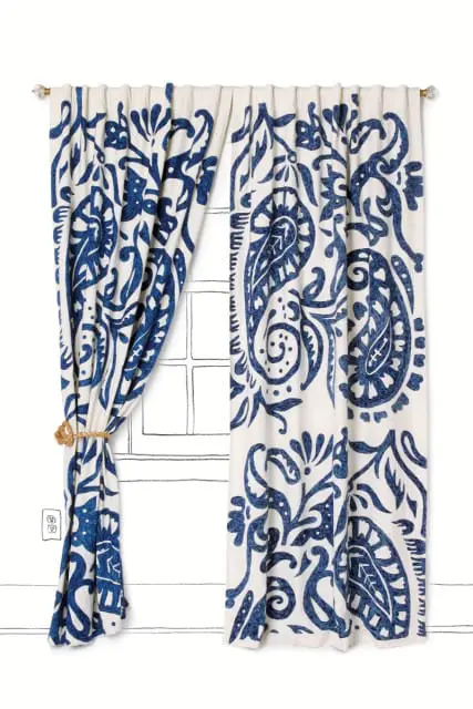 White curtains with a large-scale blue paisley and floral print, tied back with a rope tie.