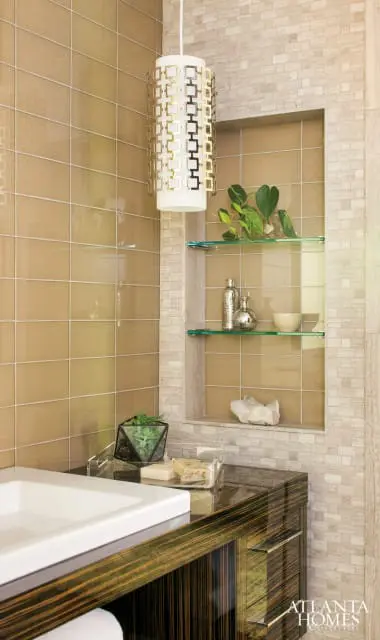 Modern bathroom with tan tiled walls, glass shelves with decorative items, and a dark wood vanity with a white sink.