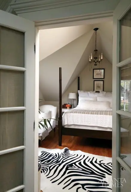 Bedroom with a dark wood four-poster bed, white bedding, and a zebra print rug. A white armchair sits near the foot of the bed.