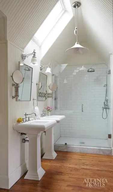 White bathroom with two pedestal sinks, a glass-enclosed shower with white subway tile, and a skylight.