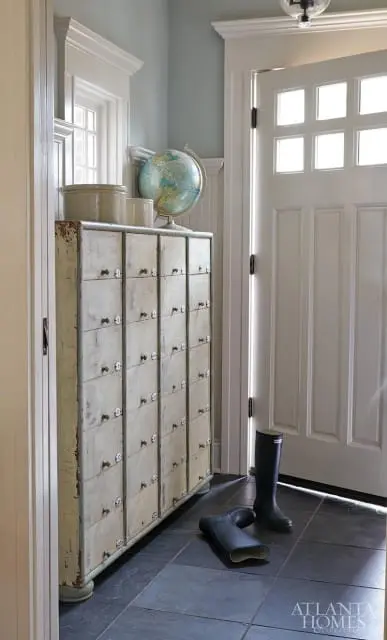 Entryway with a vintage locker cabinet, a globe, two pairs of boots, and a white paneled door with glass panes.
