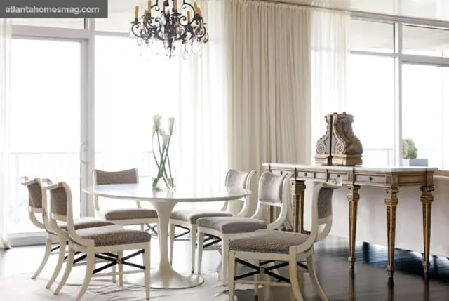 Dining room with a white tulip table, upholstered chairs with leopard print fabric, a marble-topped console table, and a crystal chandelier.