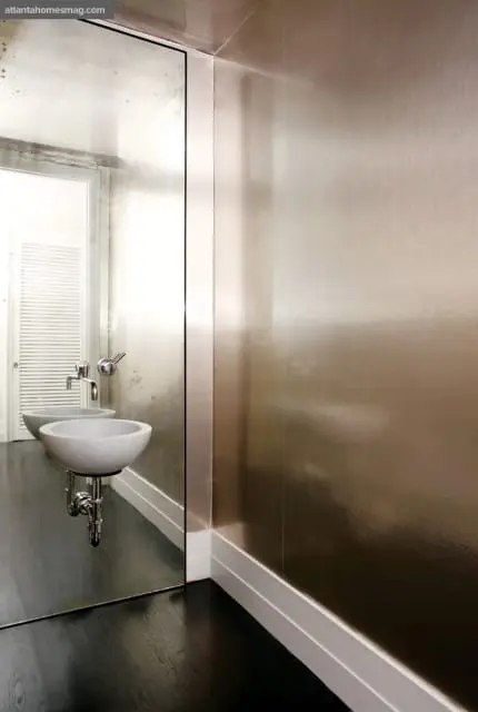 Powder room with a marble vessel sink, chrome faucet, and metallic champagne wallpaper. A large mirror reflects a louvered door and dark wood floor.