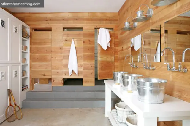 Rustic locker room with wood-paneled walls, white lockers, and a row of sinks with galvanized buckets.
