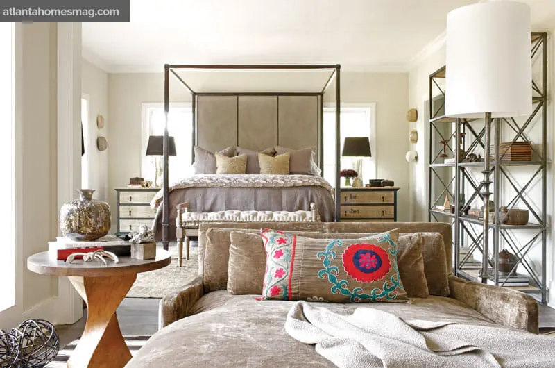 Bedroom with a four-poster bed, upholstered headboard, tufted bench, and velvet chaise lounge with decorative pillows.