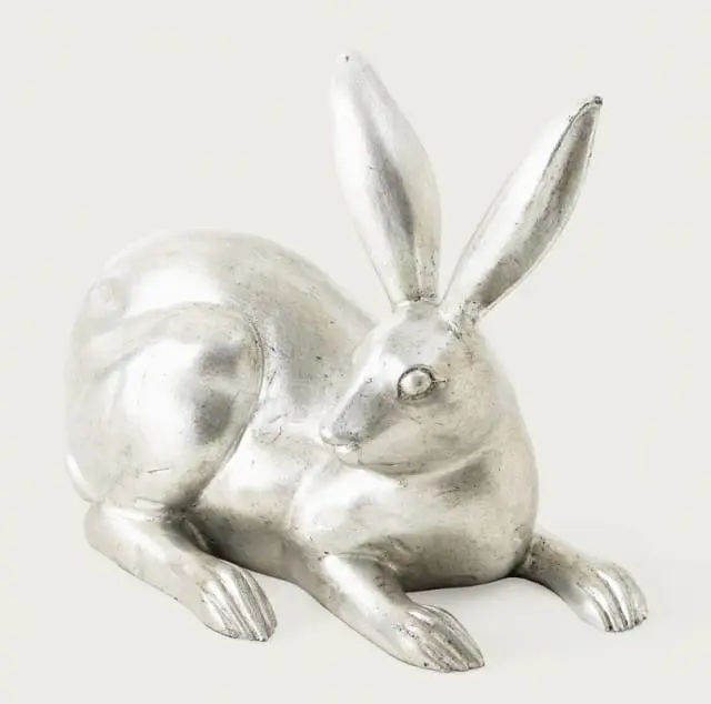 Silver sculpture of a rabbit lying down with long ears and detailed paws.