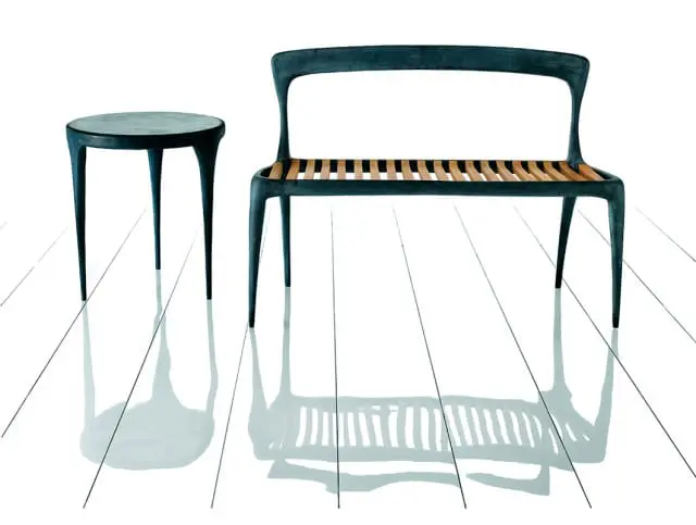 Dark grey cast metal bench with slatted wood seat and matching round side table on a white reflective floor.