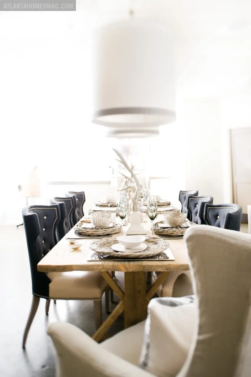 Dining room with a long wooden table set for a meal, featuring dark tufted chairs and white upholstered chairs.
