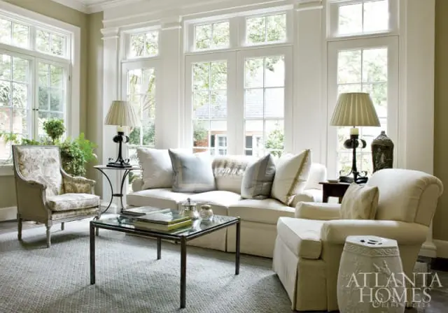 Living room with a cream sofa, two armchairs, a glass coffee table, and a patterned armchair near large windows.