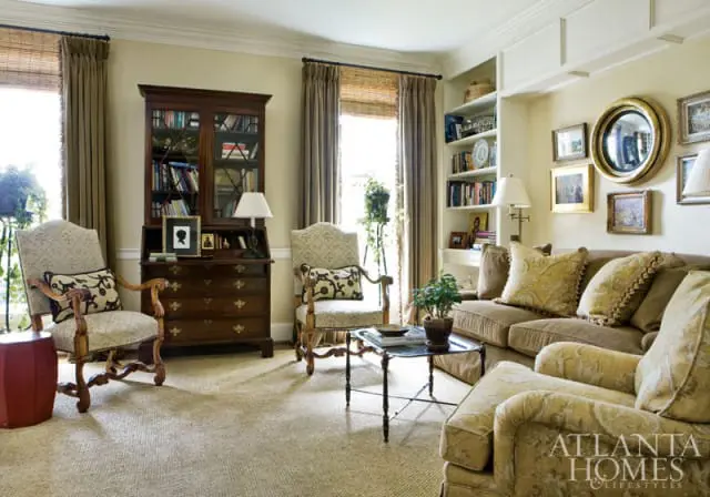 Living room with traditional furniture, including a dark wood secretary desk, upholstered chairs, and a sofa. Built-in bookshelves line the wall, adorned with framed art and a round mirror.