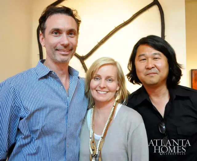 Three people posing for a photo in front of artwork. The Atlanta Homes & Lifestyles logo is in the bottom right corner.