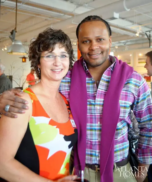 Woman with short curly brown hair and glasses wearing a colorful floral top, and a man with braided hair wearing a plaid shirt and a purple sweater draped over his shoulders.
