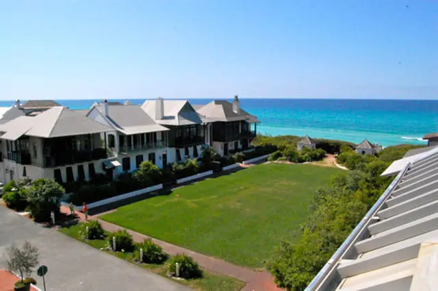 Row of coastal homes with metal roofs and porches overlooking a green lawn and the turquoise ocean