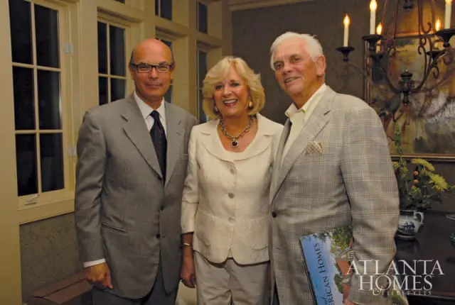 Three people posing for a photo, two men in suits and a woman in a cream-colored suit. The man on the right holds a magazine titled "Atlanta Homes & Lifestyles."
