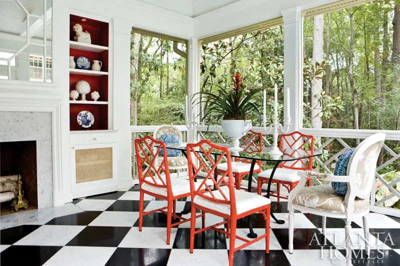 Screened porch with black and white checkered floor, glass-top dining table with orange bamboo chairs, and a fireplace with built-in shelves.