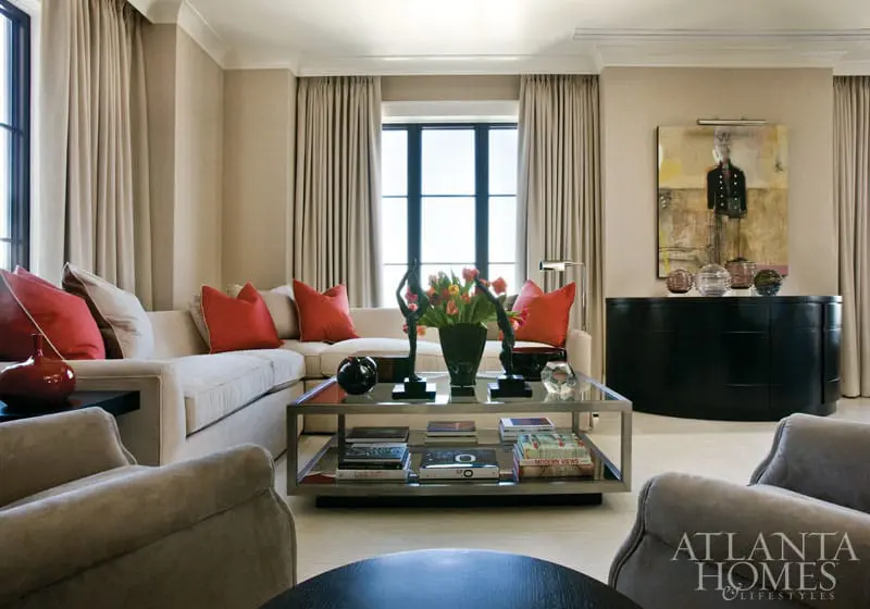 Living room with a sectional sofa, red accent pillows, glass coffee table with books, and a black credenza with artwork above.