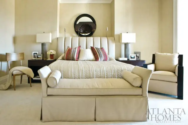 Bedroom with a king-size bed featuring a tufted headboard, striped pillows, and a textured quilt. A neutral upholstered bench sits at the foot of the bed.