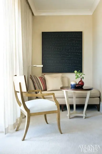 Living room seating area with a light wood armchair, a cream sofa with striped and cream pillows, and a round side table with decorative vases.