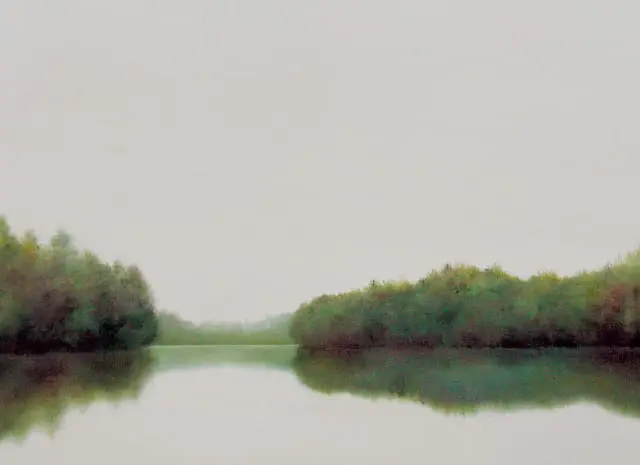 Misty lake with reflections of lush green trees on either side under a pale sky