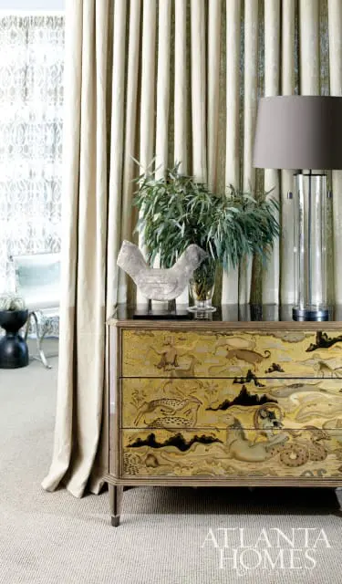 Chest of drawers with gold relief depicting mythological scenes and animals, topped with a bird sculpture and a glass lamp.