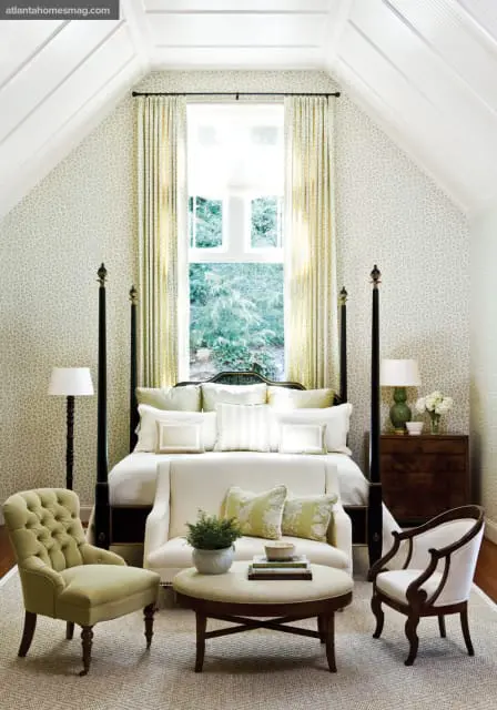 Bedroom with a four-poster bed, tufted armchair, and upholstered bench. Walls are covered in a subtle floral wallpaper, and the vaulted ceiling features white wood paneling.